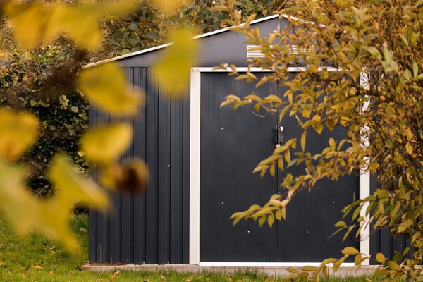 Kleines Gartengerätehaus hinter herbstlichen Blättern.